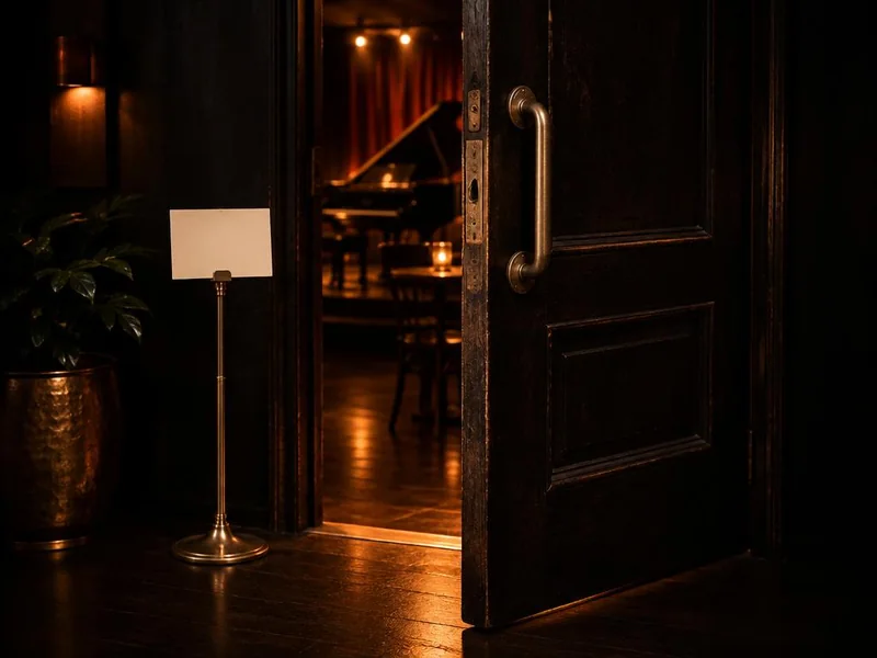 A heavy door slightly open, warm light spilling out beside a blank card on a brass holder